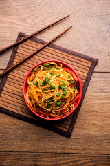 Schezwan Noodles or vegetable Hakka Noodles or chow mein is a popular Indo-Chinese recipes, served in a bowl or plate with wooden chopsticks. selective focus