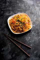 Schezwan Noodles or vegetable Hakka Noodles or chow mein is a popular Indo-Chinese recipes, served in a bowl or plate with wooden chopsticks. selective focus