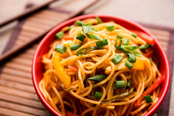 Schezwan Noodles or vegetable Hakka Noodles or chow mein is a popular Indo-Chinese recipes, served in a bowl or plate with wooden chopsticks. selective focus
