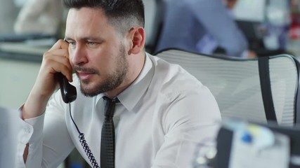 Medium shot of middle-aged man in white shirt and necktie sitting in office and talking on the phone - Powered by Adobe