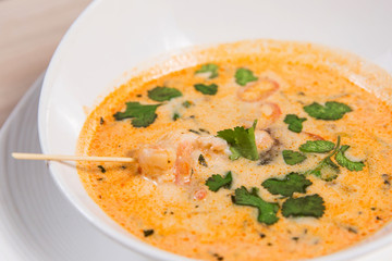 Yellow soup in with shrimps in white bowl on light wooden table in a restaurant