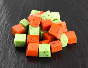 Cheese cubes of red and green color on a slate board. Cheese pesto closeup on the surface of the stone.