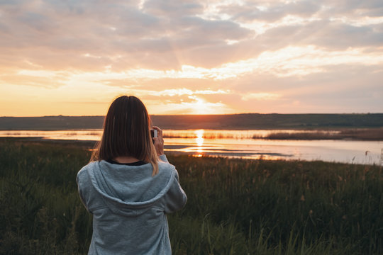 Young woman taking sunrise photos with a smartphone
