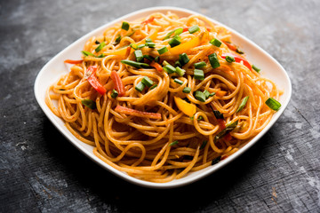 Schezwan Noodles or vegetable Hakka Noodles or chow mein is a popular Indo-Chinese recipes, served in a bowl or plate with wooden chopsticks. selective focus