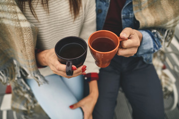 Top view of couple in love is sitting outdoor while holding cups with tea in arms