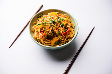 Schezwan Noodles or vegetable Hakka Noodles or chow mein is a popular Indo-Chinese recipes, served in a bowl or plate with wooden chopsticks. selective focus