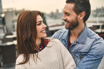 Waist up of smiling man and woman is standing on terrace and hugging