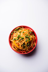 Schezwan Noodles or vegetable Hakka Noodles or chow mein is a popular Indo-Chinese recipes, served in a bowl or plate with wooden chopsticks. selective focus