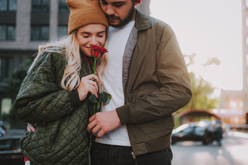 Beautiful young lady enjoying aroma of flower while standing with bearded man
