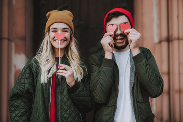 Romantic mood. Waist up portrait of charming girl in hat and cheerful bearded man covering nose and...