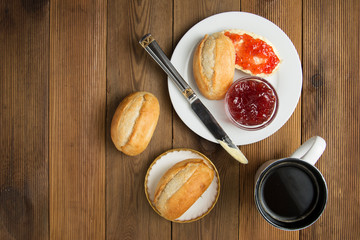 Breakfast food with coffee. Fresh buns with butter and jam on wooden background. Top view. Copy space.