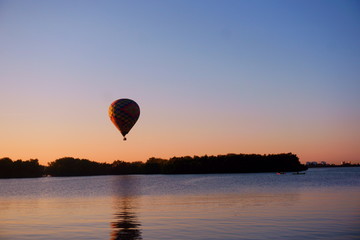 Fototapeta premium paisaje al amanecer con globo aerostático de colores sobre colinas y lago