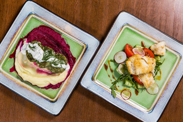 Fish with vegetables and sauces in square plates on wooden table in luxury restaurant