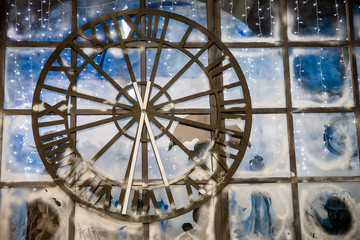 Closeup image of decorated Christmas interior at wall with big clock background.Old rusty big street clock on wall of the building,hotel, store.Old metal clock hanging on the transporent wall.