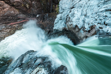 The rushing force of a waterfall catches the green of the lush rain forest and white water on an overcast day