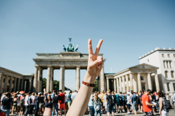 The girl shows peace sign on the background of the Brandenburg Gate and blurred unrecognizable...