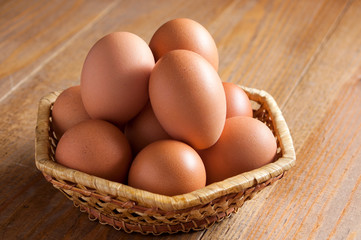 Brown chicken eggs lies in a wicker basket on a wooden table. The background is out of focus.