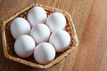 White chicken eggs lie in a wicker basket on a wooden table.