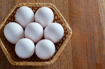 White chicken eggs lie in a wicker basket on a wooden table. View from above.