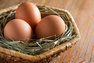 Three large fresh brown eggs in a wicker basket.