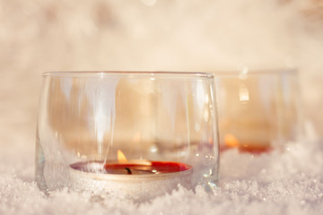 Two candles in the glasses on the snow.