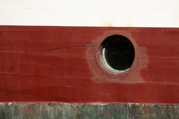 Porthole on the red wall of the old ship