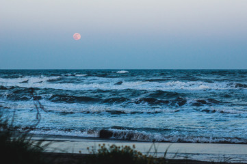 wild sea with full moon in background, focus on big waves at the beach.