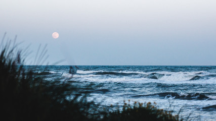 wild sea with full moon in background, focus on big waves at the beach.