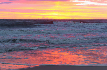 Sunset over the sea. Reflection of sunlight in the sea waves. Red and yellow sky in the rays of the sunset.