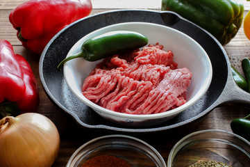 Raw ground beef inside skillet with peppers and other cooking ingredience around