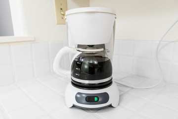 Small white coffee maker on clean white tile kitchen counter.  