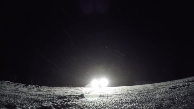 Car at night in the snow. Light headlights, glare. A snowstorm, snowflakes fall in the rays of light. Blizzard on the highway, bad weather in winter. Road traffic safety at night