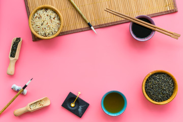 Fototapeta na wymiar Chinese traditional symbols concept. Tea, rice, hieroglyph love, bamboo table mat, chopsticks, soy sause on pink background top view frame copy space