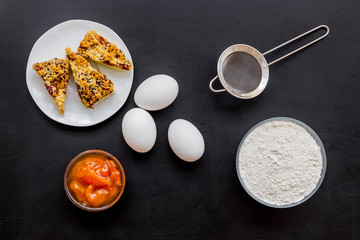 Cook cookies at home concept. Ingredients and instruments for make cookies. Fresh cookies near flour, eggs and sieve on black background top view