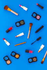 visagiste desk with decorative cosmetics: eyeshadows, lipstick, brush blue background top view