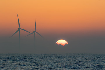Offshore wind turbines. Misty morning sea sunrise. Tropical background landscape.