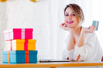 Young girl with holiday gifts and laptop computer holding a credit card. Business, education, shopping and other concept