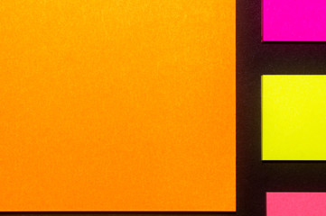 Yellow, orange and rose hue colorful office stickers on black paper. Office noteparer as reminder. Isolated on black paper.