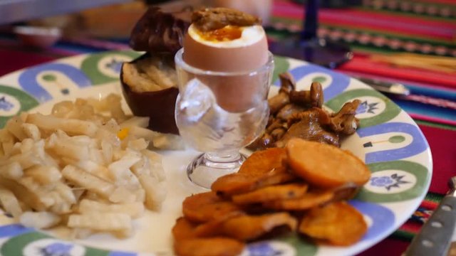 A plate in a restaurant with a semi-calf egg, sweet potato frittes and celery root. The plate is placed on a coloured tablecloth.