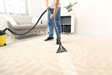 Man removing dirt from carpet with vacuum cleaner in room