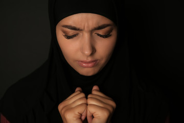 Portrait of sad Muslim woman in hijab  praying on dark background