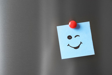 Note with funny face on refrigerator door. Space for text
