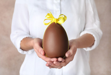 Woman holding chocolate Easter egg with bow knot on color background, closeup