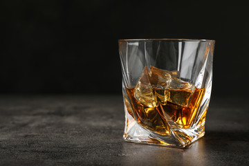 Golden whiskey in glass with ice cubes on table. Space for text