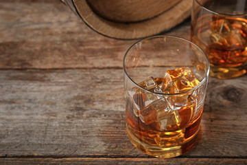 Golden whiskey in glass with ice cubes on wooden table. Space for text
