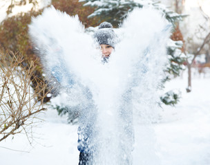 cute young boy in orange hat blue jacket plays with snow, has fun, smiles. Teenager rises his hands up in winter park. Active lifestyle, winter activity, outdoor winter games, snowballs. blurred snow