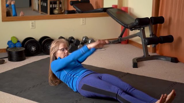 Pretty, mature woman doing situps in a home exercise area.