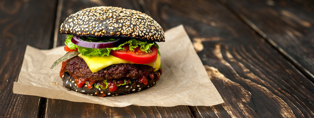 Beef hamburger with black bun with lettuce and ketchup served on a rustic wooden table