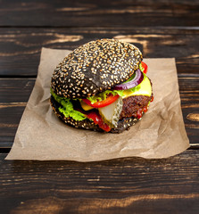 Beef hamburger with black bun with lettuce and ketchup served on a rustic wooden table
