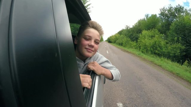 Good mood. Happy joyful teen boy rides travels in the car with the window open. Summer romantic adventures and trips, childhood memories and dreams. Headwind blowing in face